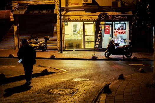 Dimly lit city street at night with a silhouette and glowing shopfront.
