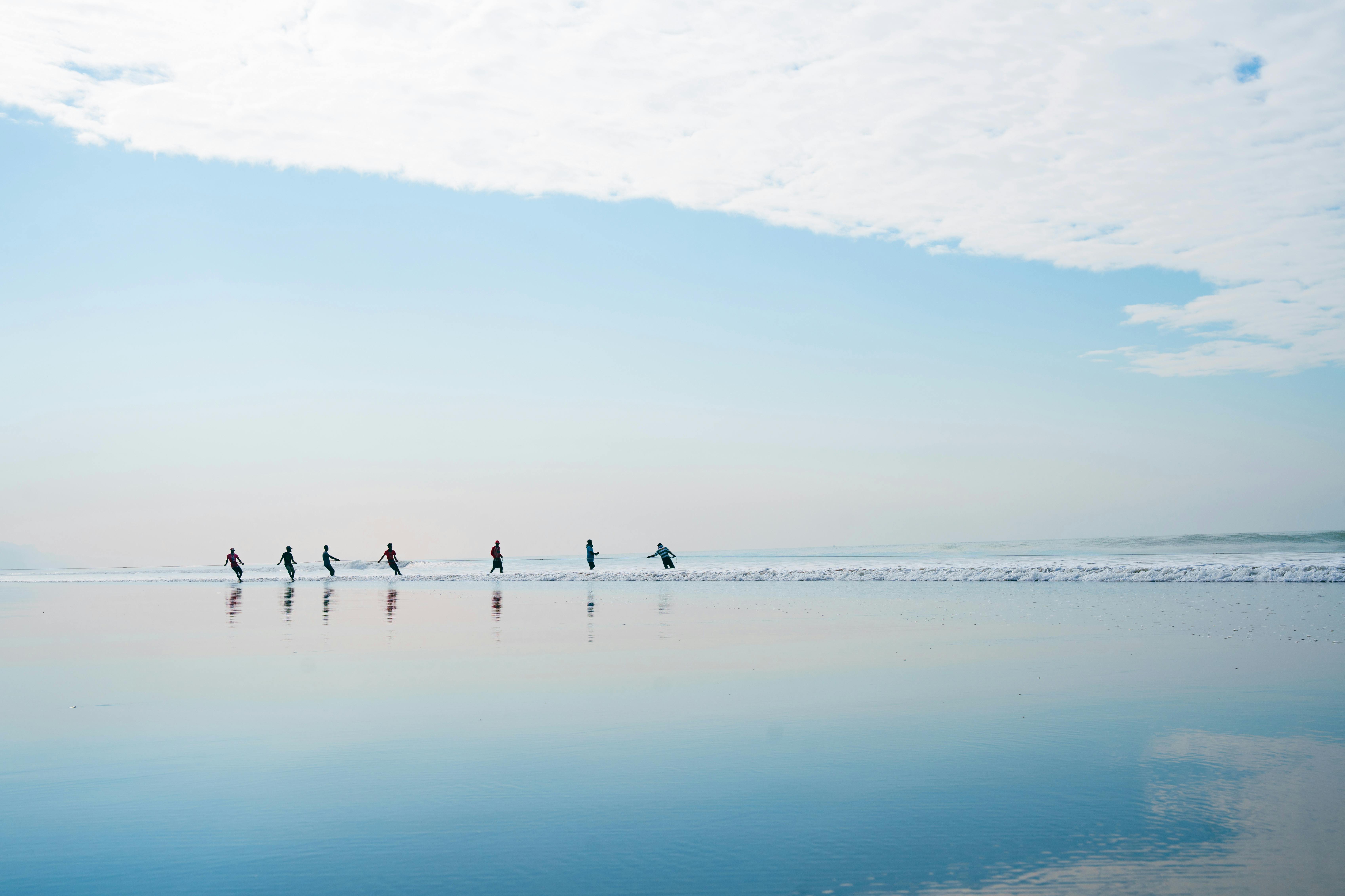 A group of people running in shallow ocean waters with a clear blue sky overhead.