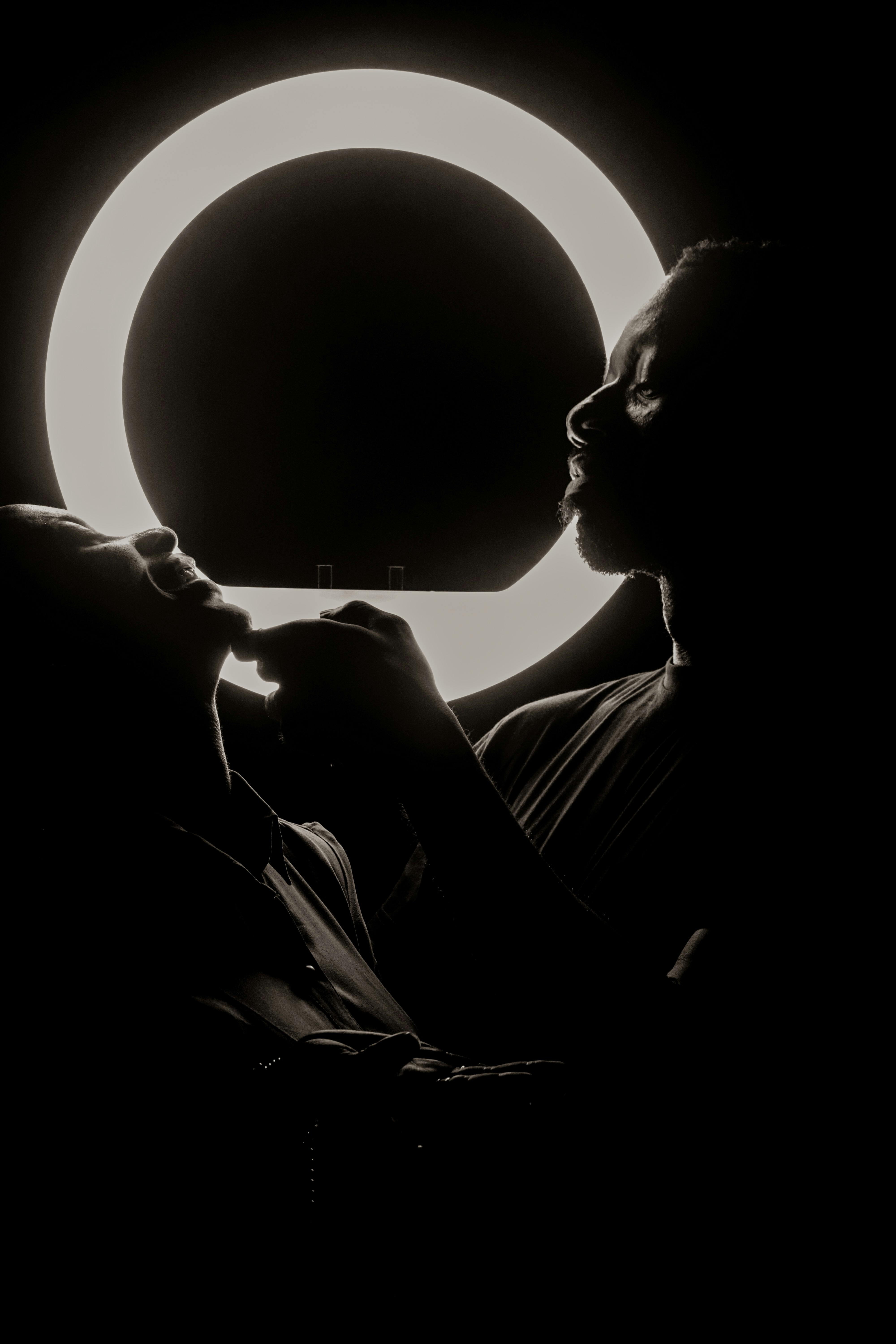Dramatic silhouette of two adults near a neon light circle.