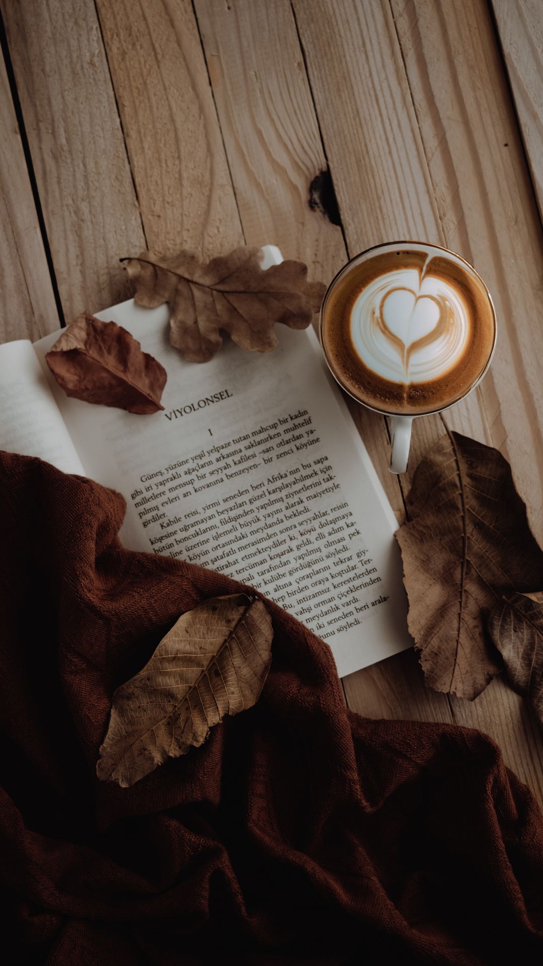Latte art next to an open book and autumn leaves on a wooden table wallpaper
