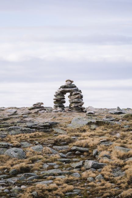 Stone cairn on a desolate rocky mountain landscape under an overcast sky.