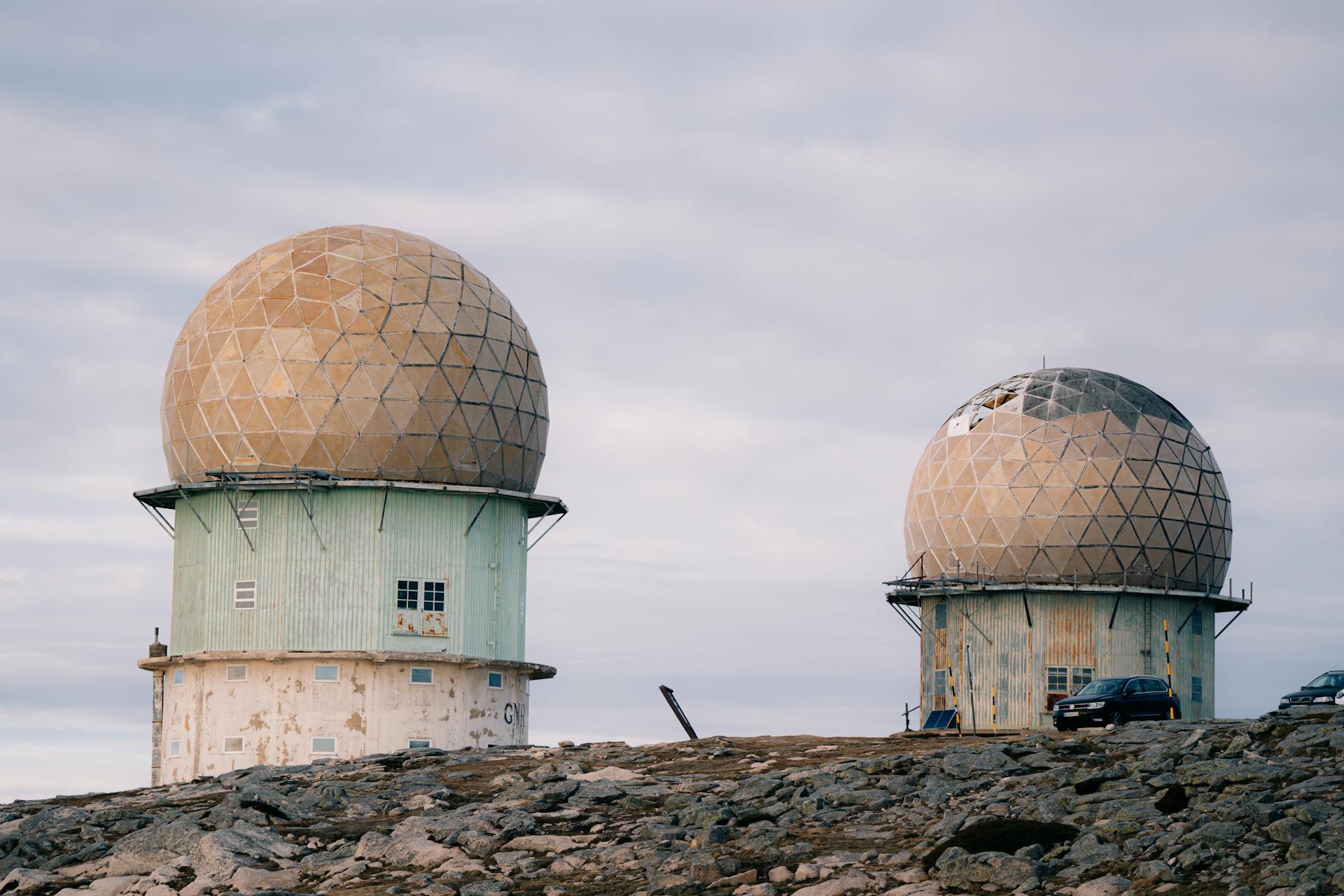 Two large geodesic radar domes stand on an abandoned military base against a cloudy sky.