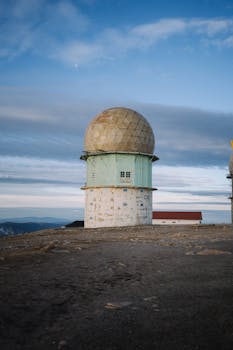 Isolated radar dome on a mountain captured during daytime under a vast sky.