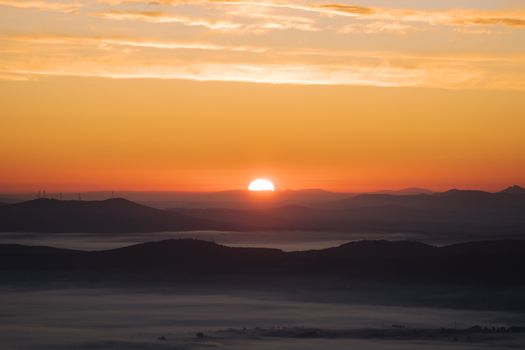 Tranquil sunrise over misty mountain valleys with vibrant sky hues.
