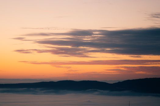 Beautiful sunrise over mountains with glowing clouds and foggy valleys.