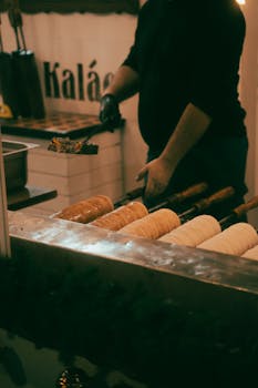 Vendor cooking traditional chimney cakes at a market stall in Cluj-Napoca, Romania.