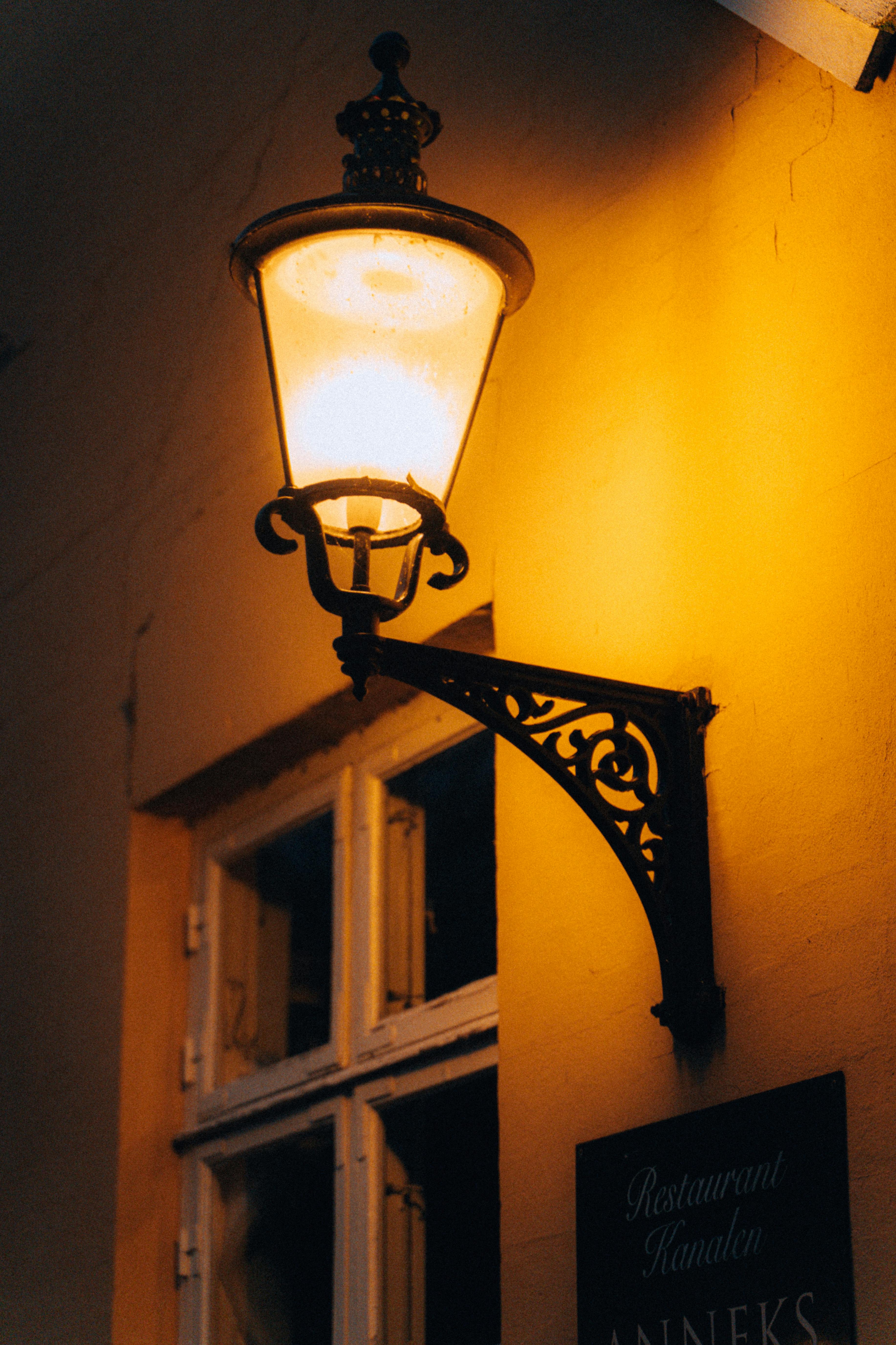 Free A glowing vintage street lamp casting a warm light on a historic Copenhagen street corner. Stock Photo