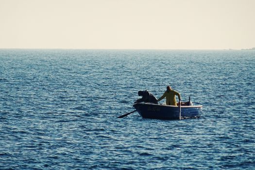 A lone person fishing in a small boat on a tranquil sea under a clear sky.