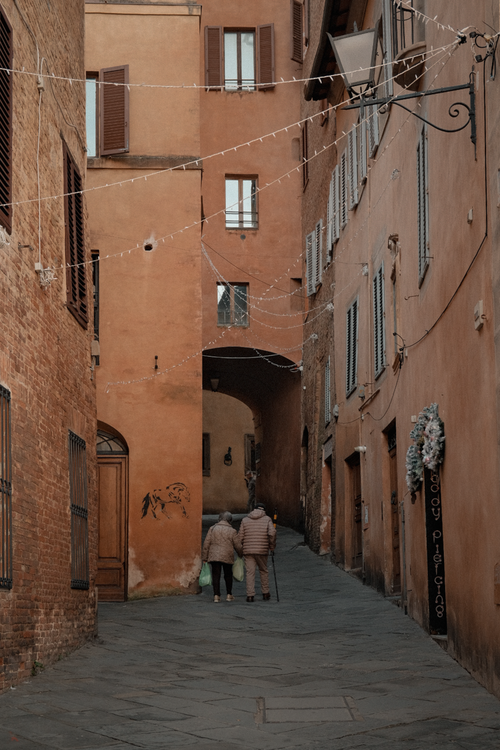 Free Cobblestone alley in historic town with two senior adults walking, autumn vibe. Stock Photo