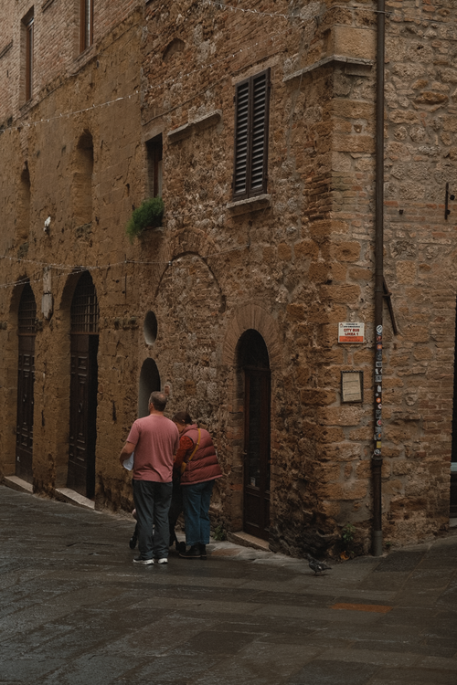 Free A couple stands by a historic stone building on a quaint street, capturing a moment of history and romance. Stock Photo