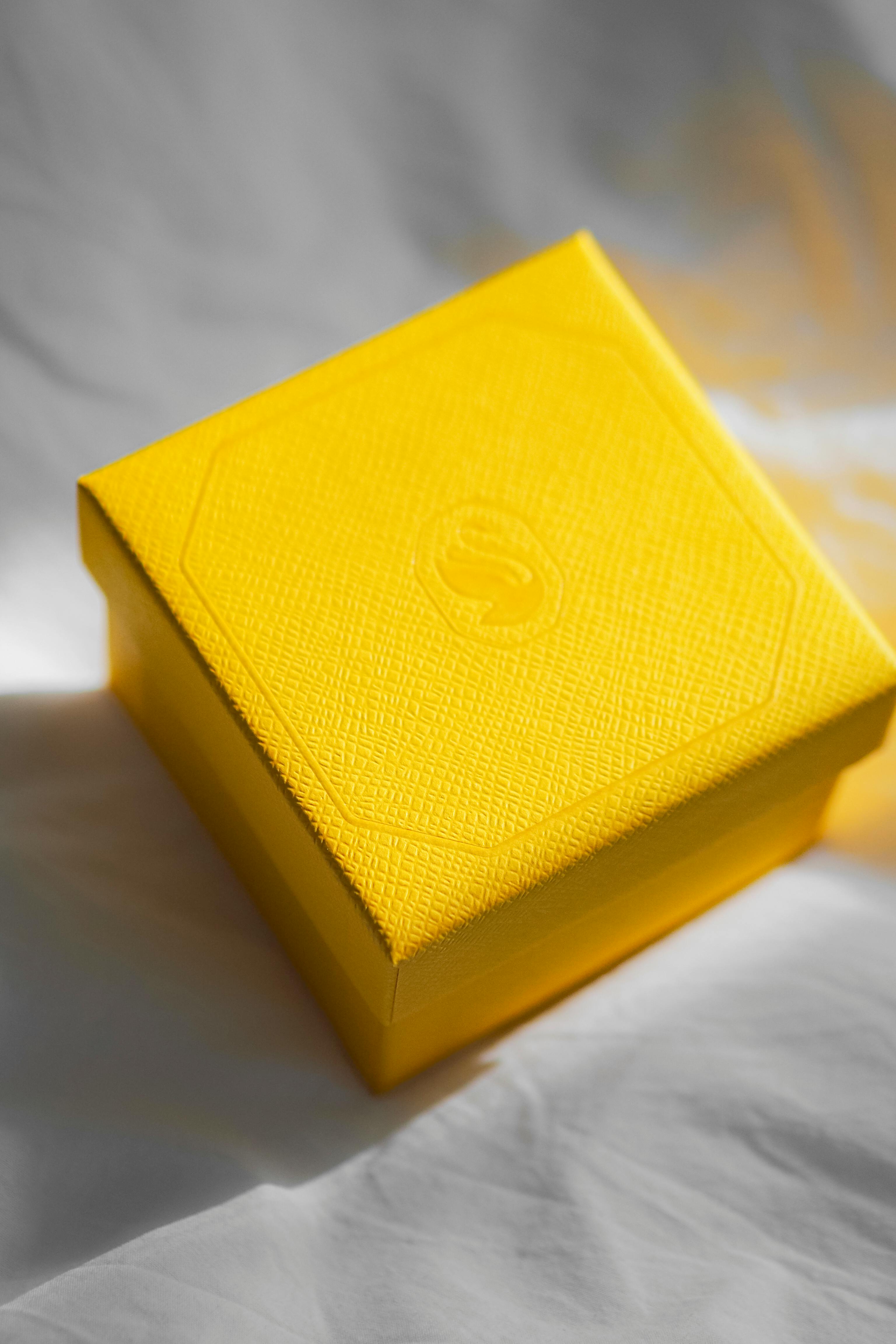 Bright yellow gift box on white fabric with sunlight highlighting its texture.