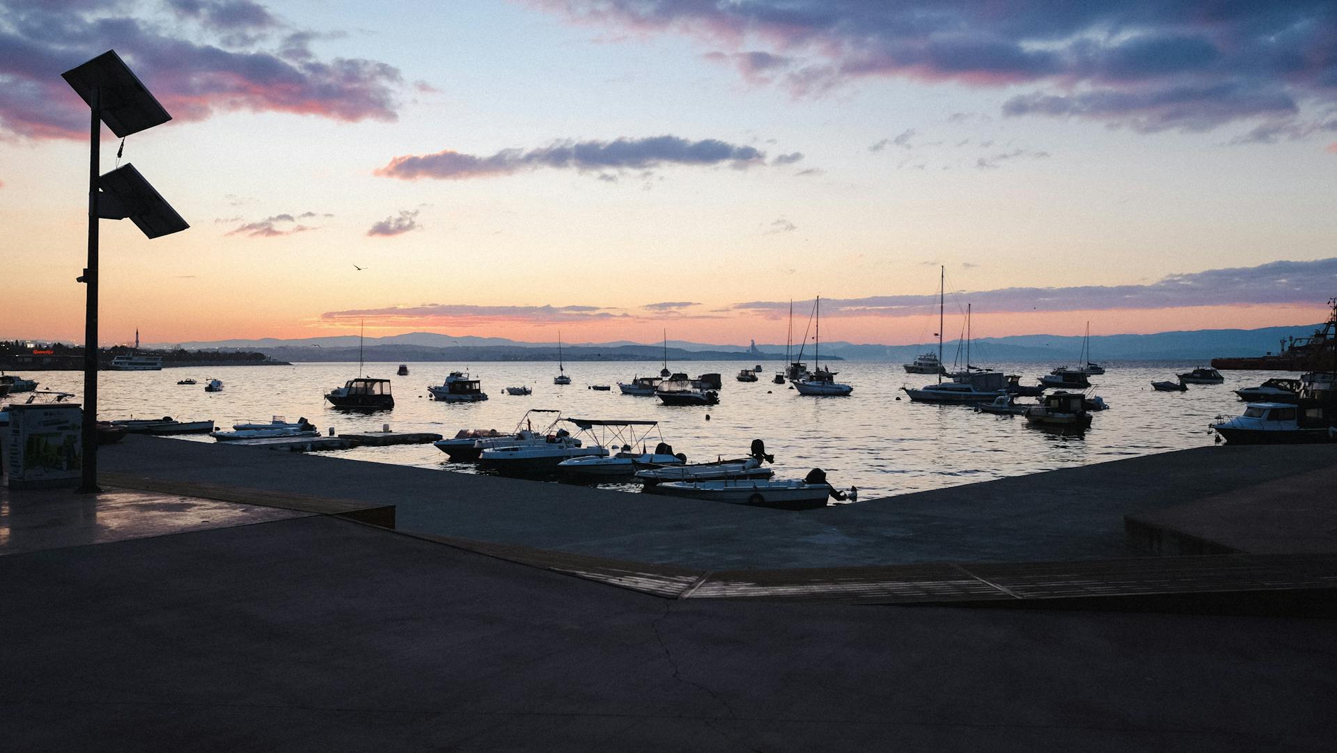 Tranquil sunrise over a harbor with boats gently floating on calm waters.