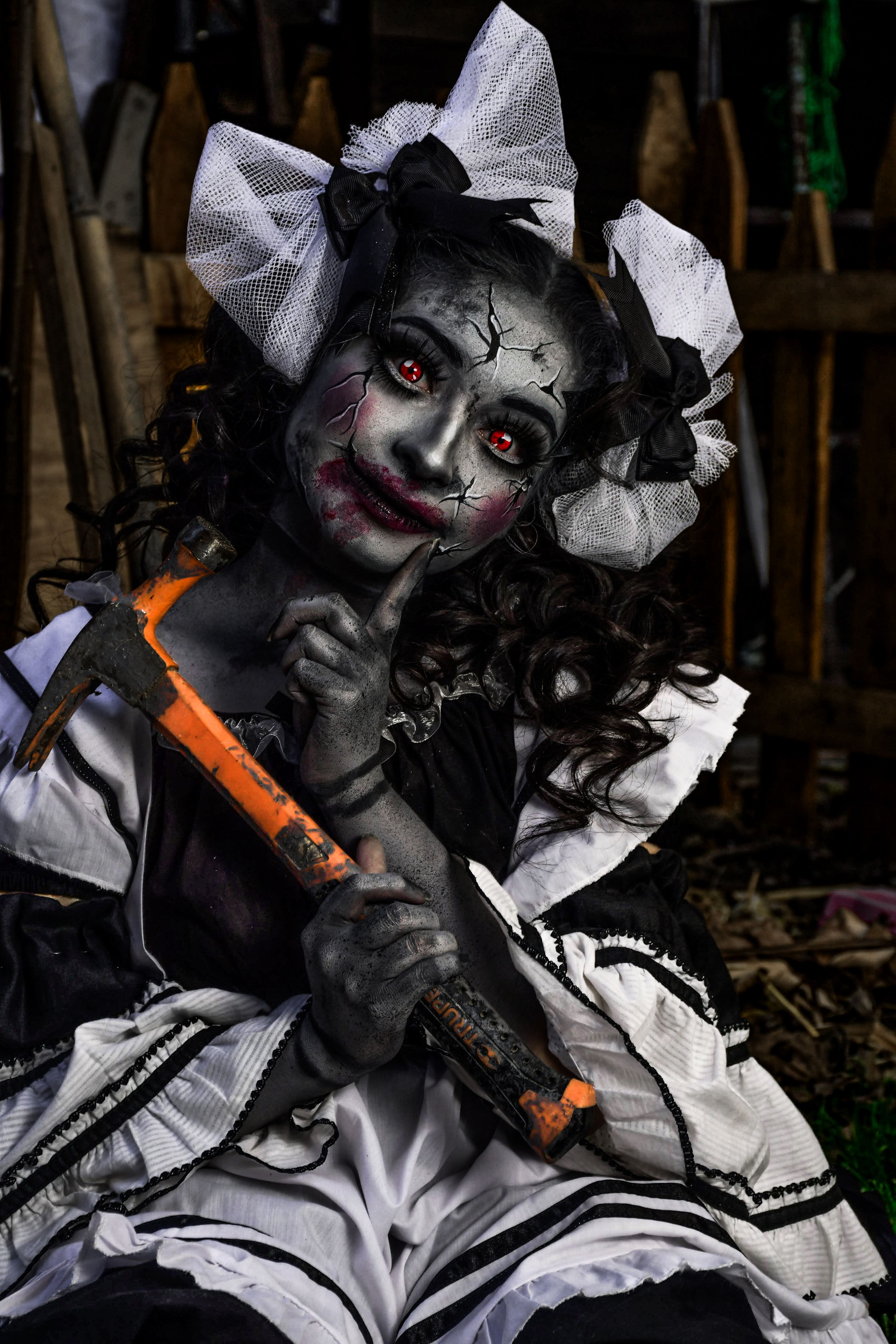 Creepy doll-like figure in vintage costume holding a hammer outdoors.