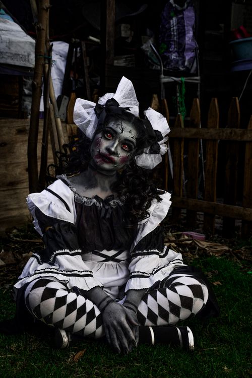 Free Woman dressed as a gothic doll sitting in a dark, eerie outdoor setting. Stock Photo