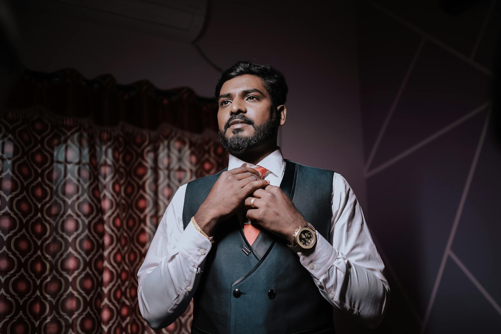 Handsome Indian groom adjusting tie in a stylish suit indoors. Perfect for wedding collections.