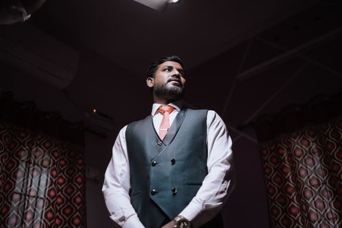 Free Portrait of a groom in a blue vest indoors with ambient lighting and colorful curtains. Stock Photo