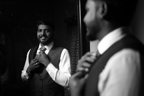 Free A groom adjusting his tie in front of a mirror, captured in elegant black and white. Stock Photo