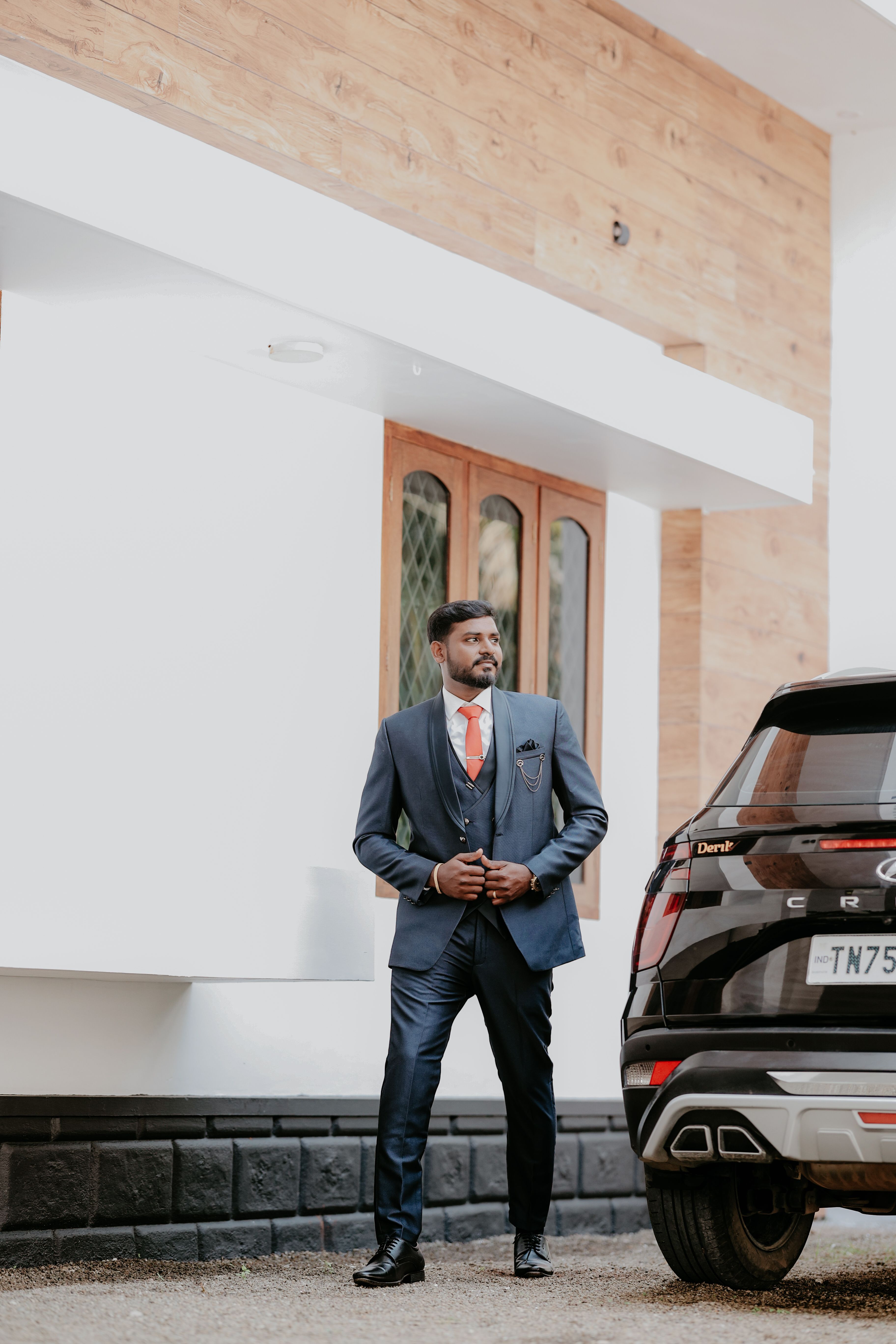 Stylish Indian groom in a blue suit standing confidently outdoors by a stylish car.