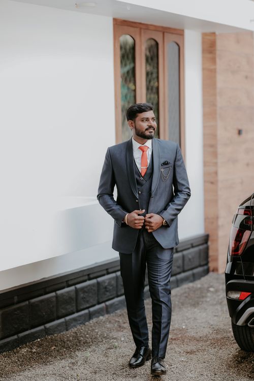 Free Stylish groom in a navy blue suit with orange tie walks confidently outside an Indian venue. Stock Photo