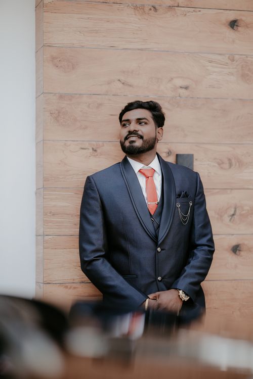 Free A stylish groom posing confidently in a blue suit with a red tie against a wooden backdrop. Stock Photo