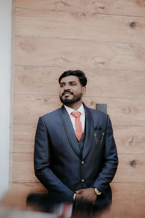 Free Stylish groom in a blue suit with red tie posing confidently against a wooden background. Stock Photo
