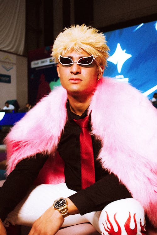 Free Person in bold attire with pink fur, sunglasses, and striking pose indoors. Stock Photo