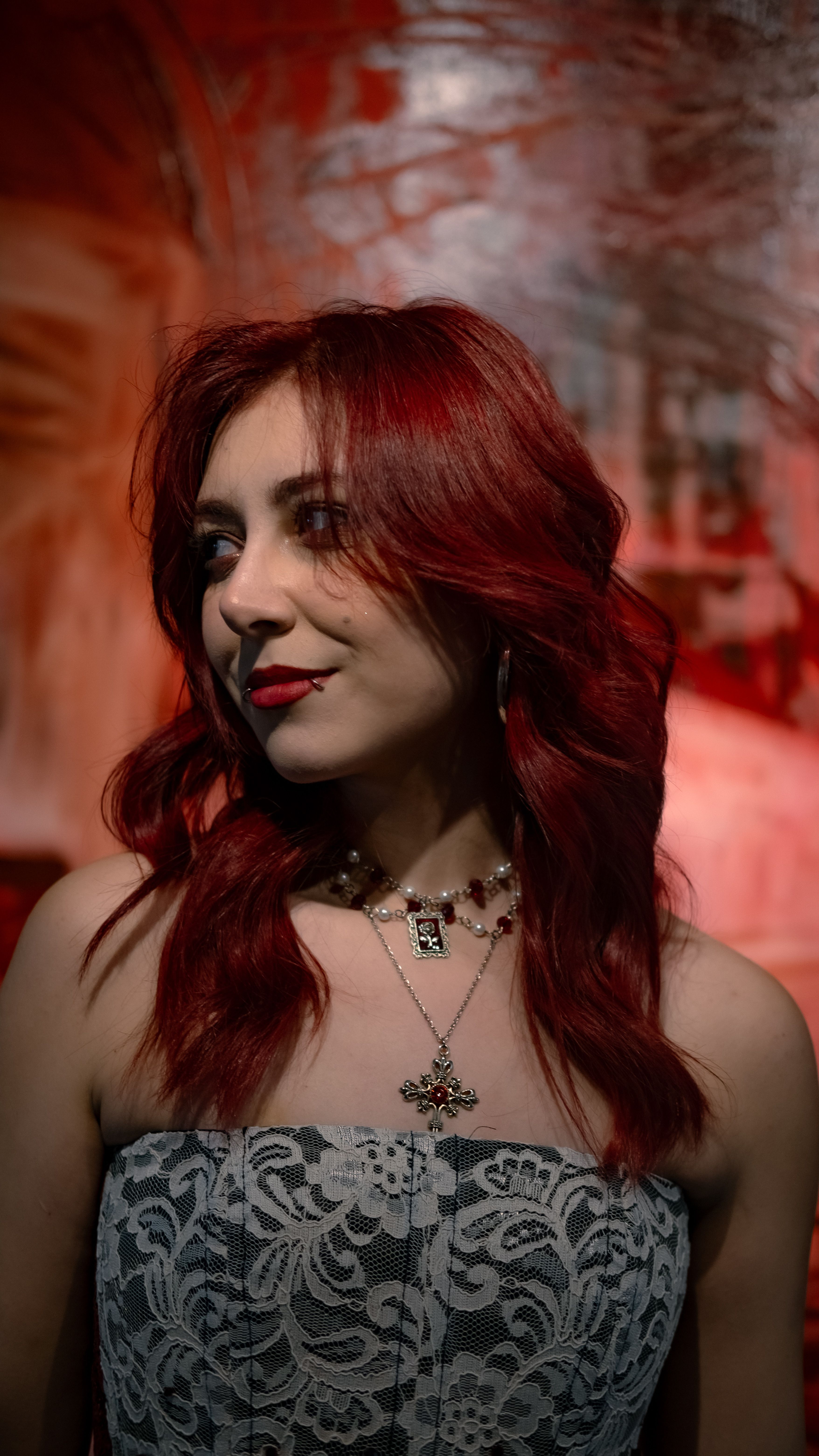 Portrait of a red-haired woman wearing a lace dress, with artistic red background.