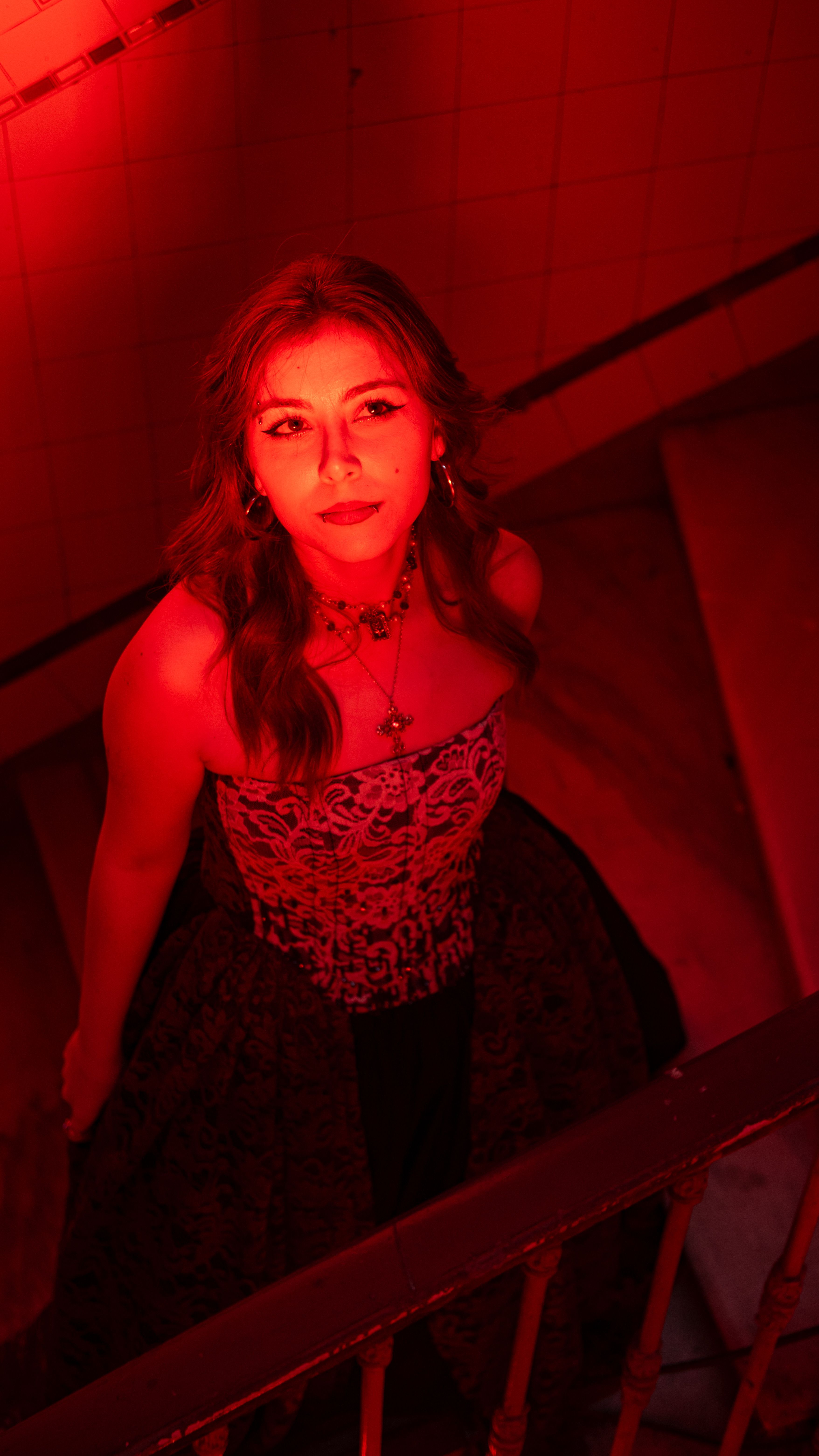A woman in elegant attire illuminated by red light on stairway.