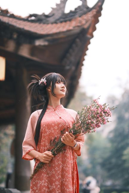 Young woman in traditional Vietnamese attire holding flowers outside a pagoda.
