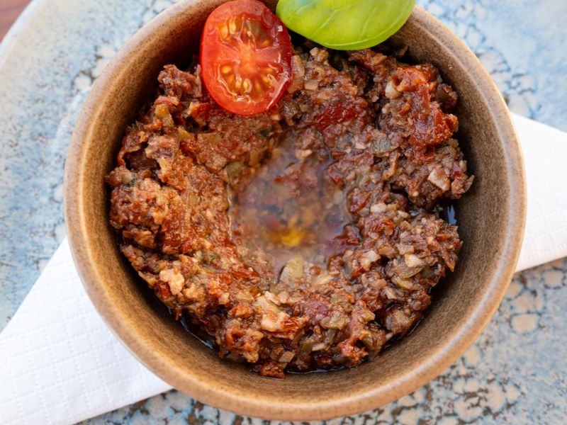 Close-up of tapenade with a cherry tomato garnish in a rustic ceramic bowl.