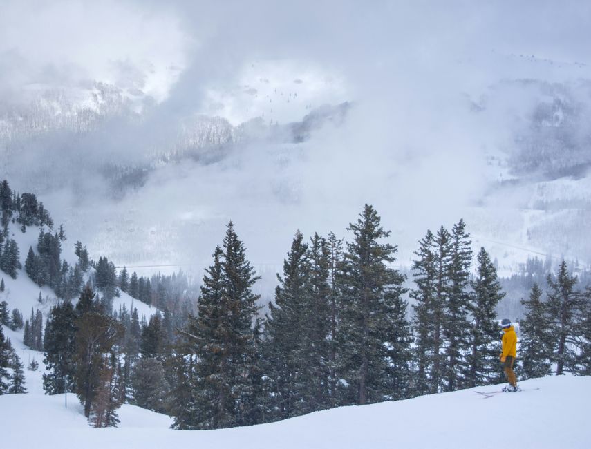 A skier in a yellow jacket enjoys a snowy day at Brighton Resort, Utah's alpine landscape.