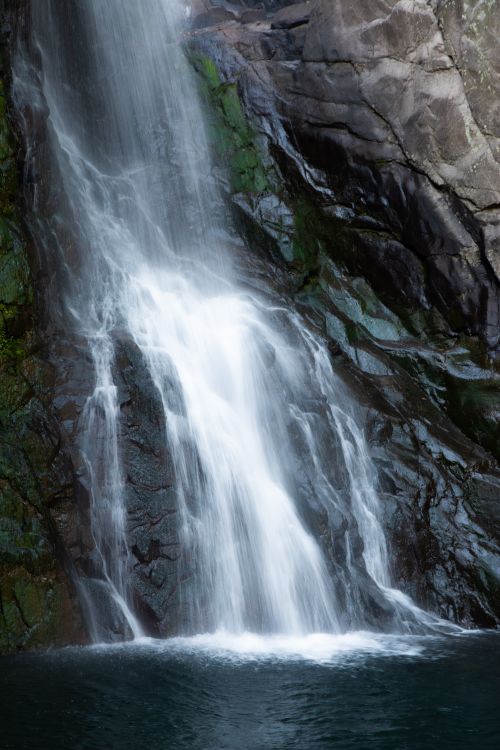 Free A tranquil waterfall flows over mossy rocks into a serene pool. Stock Photo
