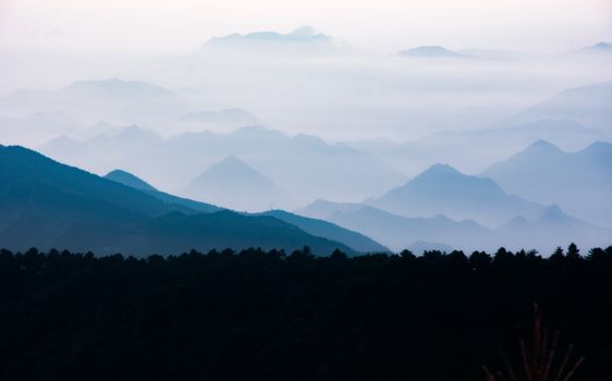 A serene view of layered mountains enveloped in mist, creating a mystical atmosphere.