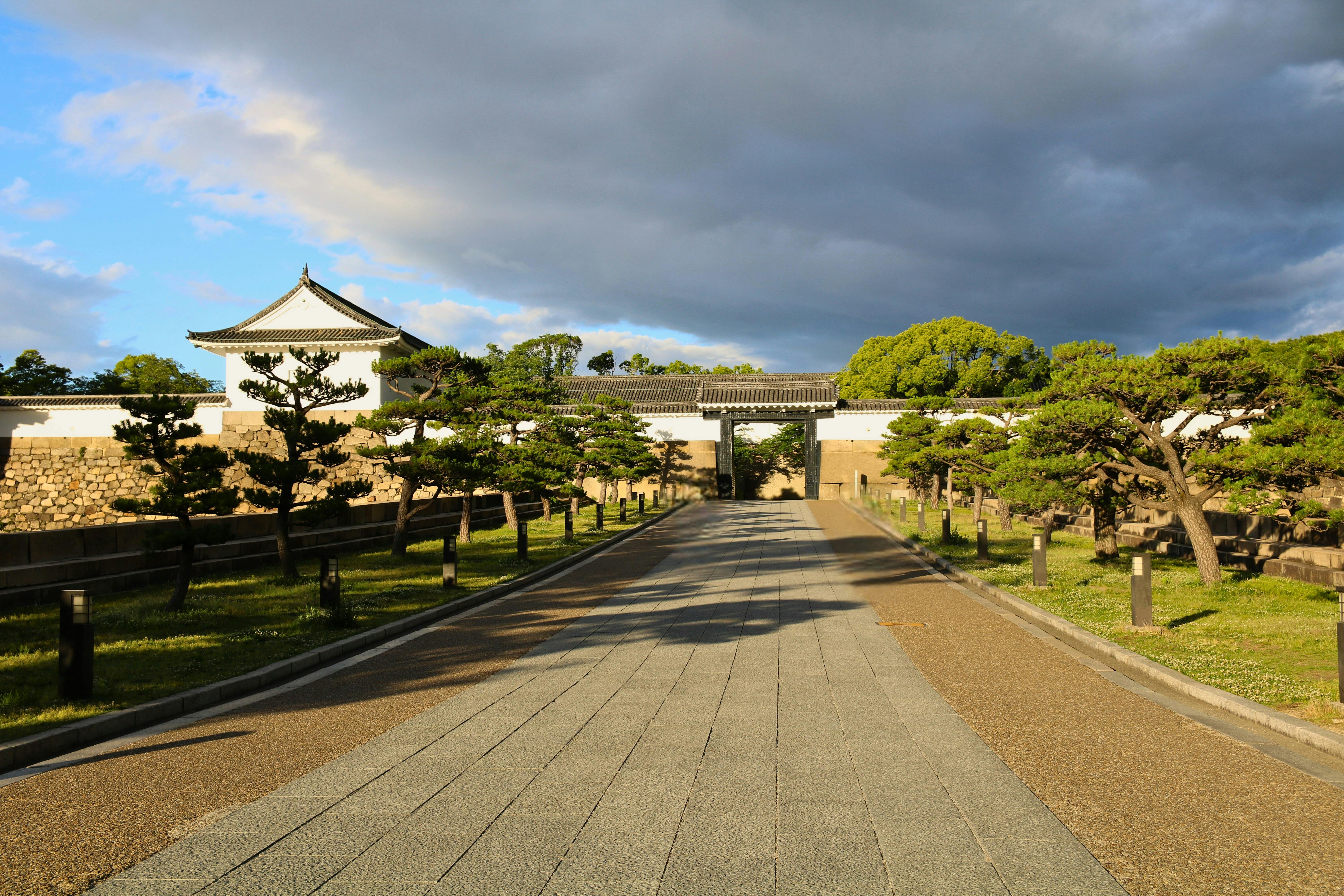 Sunny pathway leading to Osaka Castle with dramatic clouds and vibrant greenery, showcasing serene beauty.