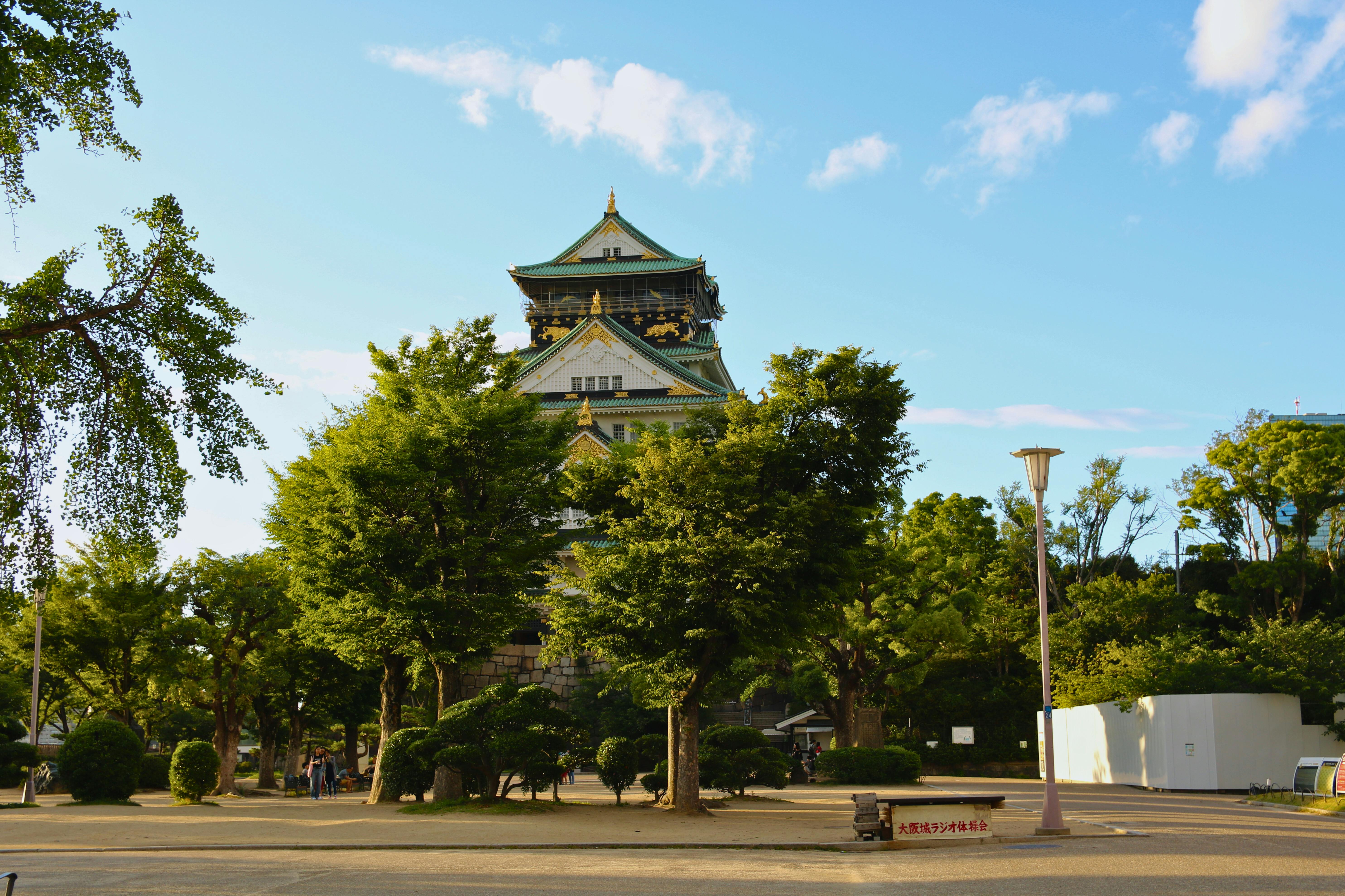 Explore the historic Osaka Castle surrounded by vibrant greenery, set against a clear blue sky. - Osaka