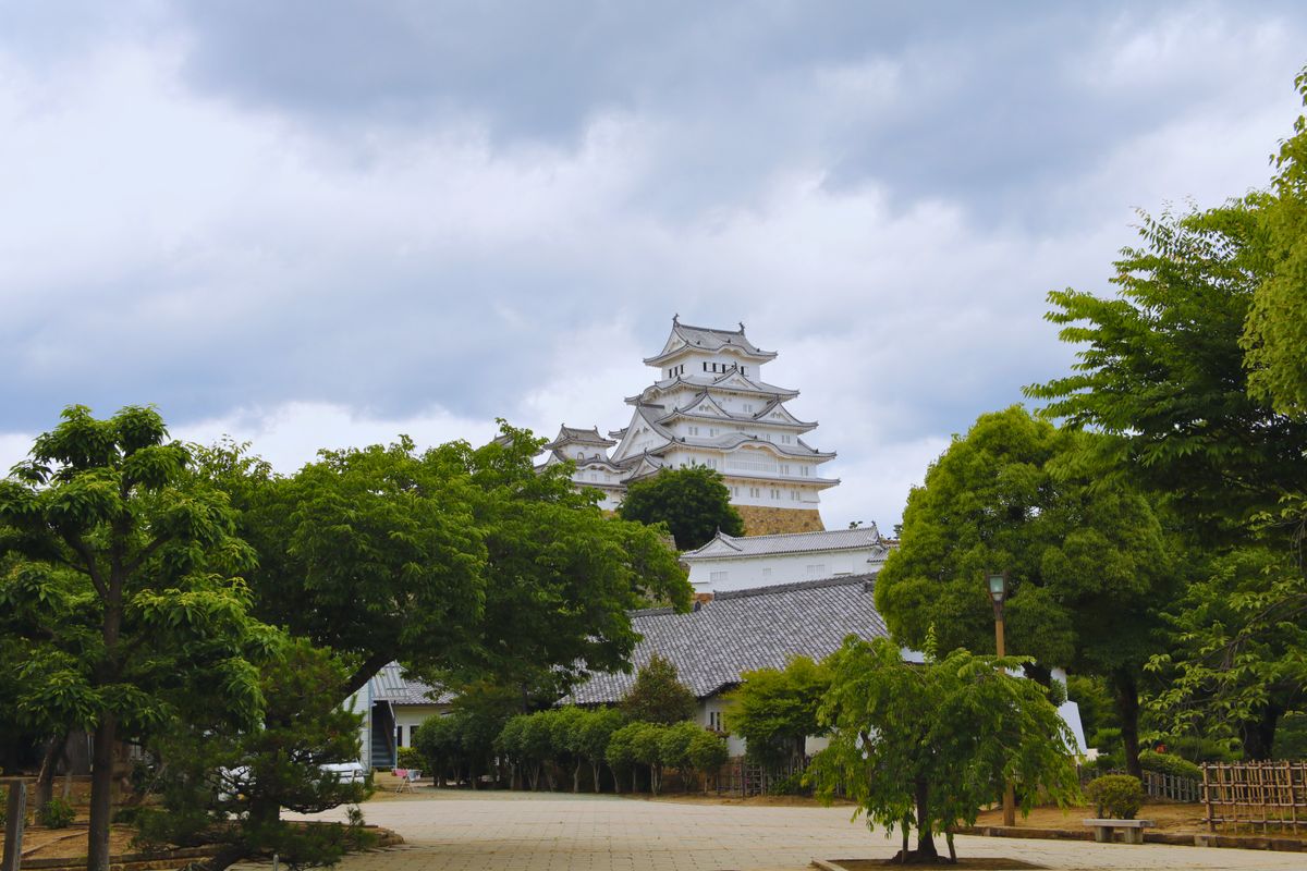 A Japanese castle keep rising above lush green trees on a hillside