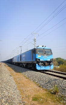 A blue cargo train traveling on tracks in Greater Noida, India, with clear sky.