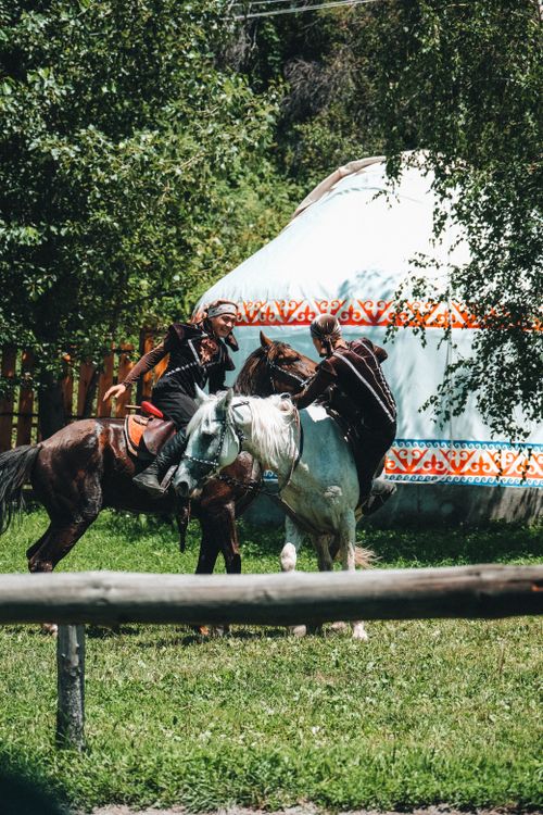 Free Two horsemen in traditional attire engage near a yurt in a lush outdoor setting. Stock Photo