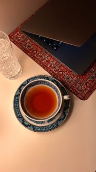 Tea cup with laptop on a decorative mat, creating a cozy workspace vibe.