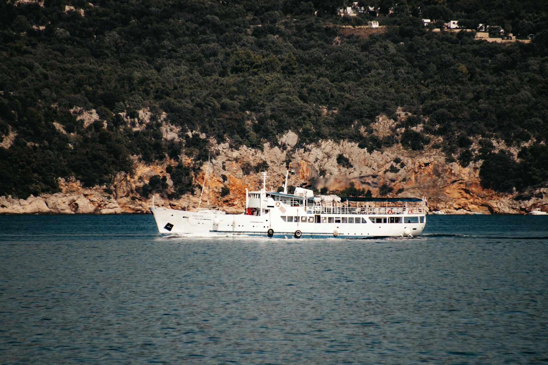 A ferry cruises through the Adriatic Sea near Lopud Island, Croatia, showcasing stunning natural cliffs.
