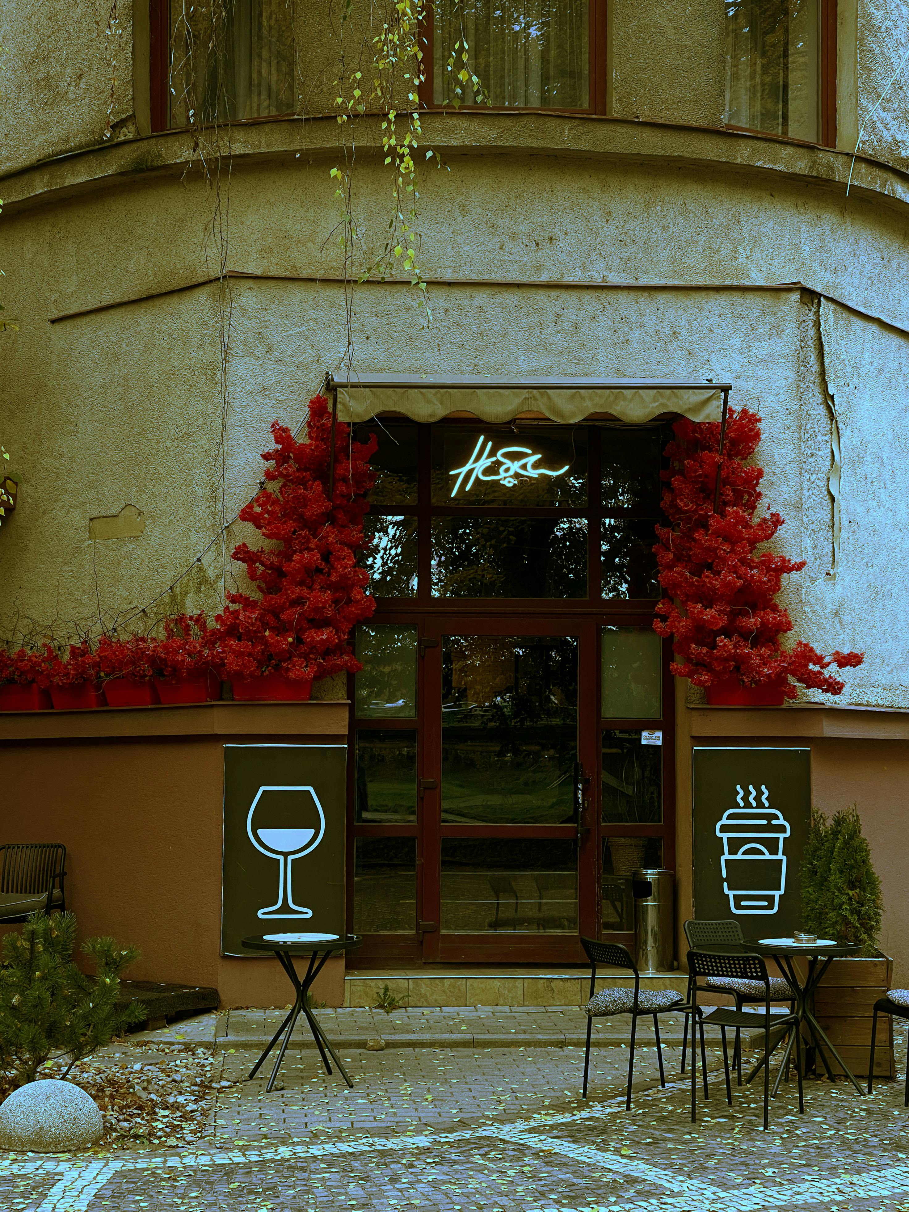Charming cafe entrance adorned with red foliage and modern neon signs.