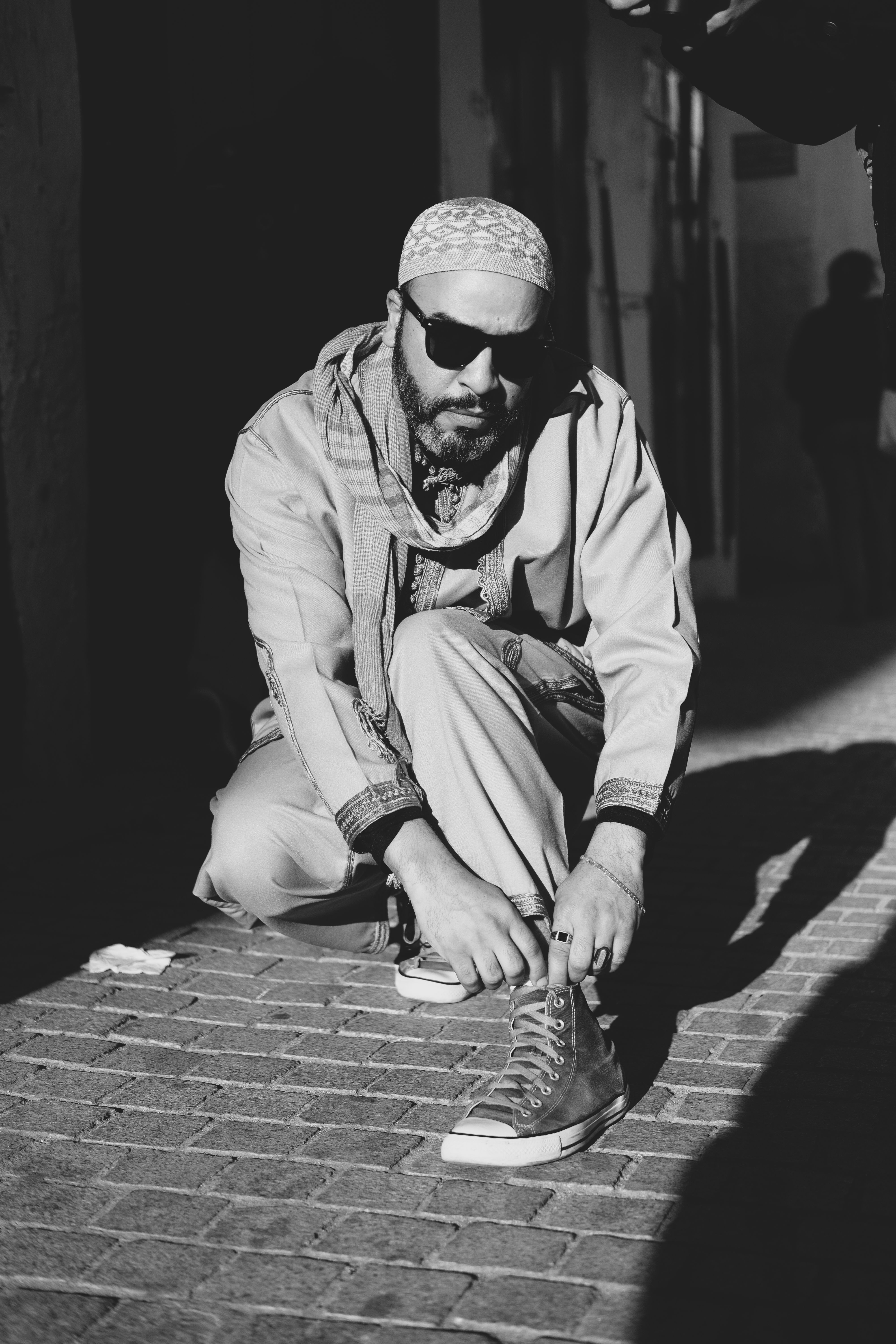 Black and white photo of a man tying shoelaces in Rabat, Morocco's charming streets.