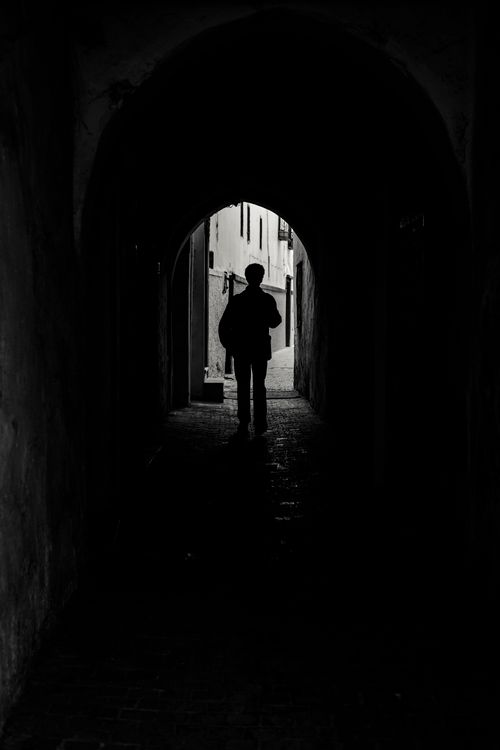 Free Moody black and white photo of a silhouette walking through a narrow passageway in Rabat's medina. Stock Photo