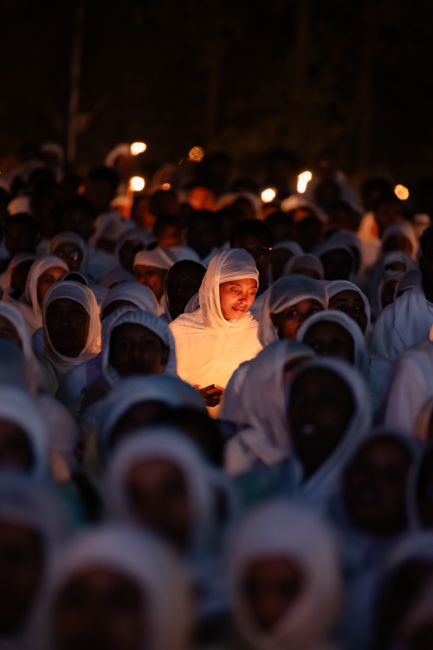 Young girl participates in Ethiopian Orthodox candlelight vigil, surrounded by worshippers in traditional attire.