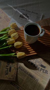 A cozy scene with a coffee mug, tulips, and vintage newspapers on a sunny morning.