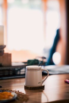 A mug with 'JOY' text on a sunny table evokes a cozy morning vibe.