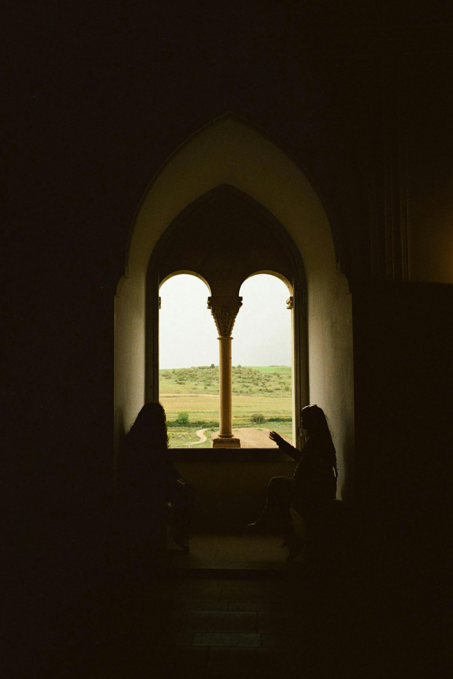 Silhouettes conversing by a window in Alcázar of Segovia, with scenic views of Spain's landscape.