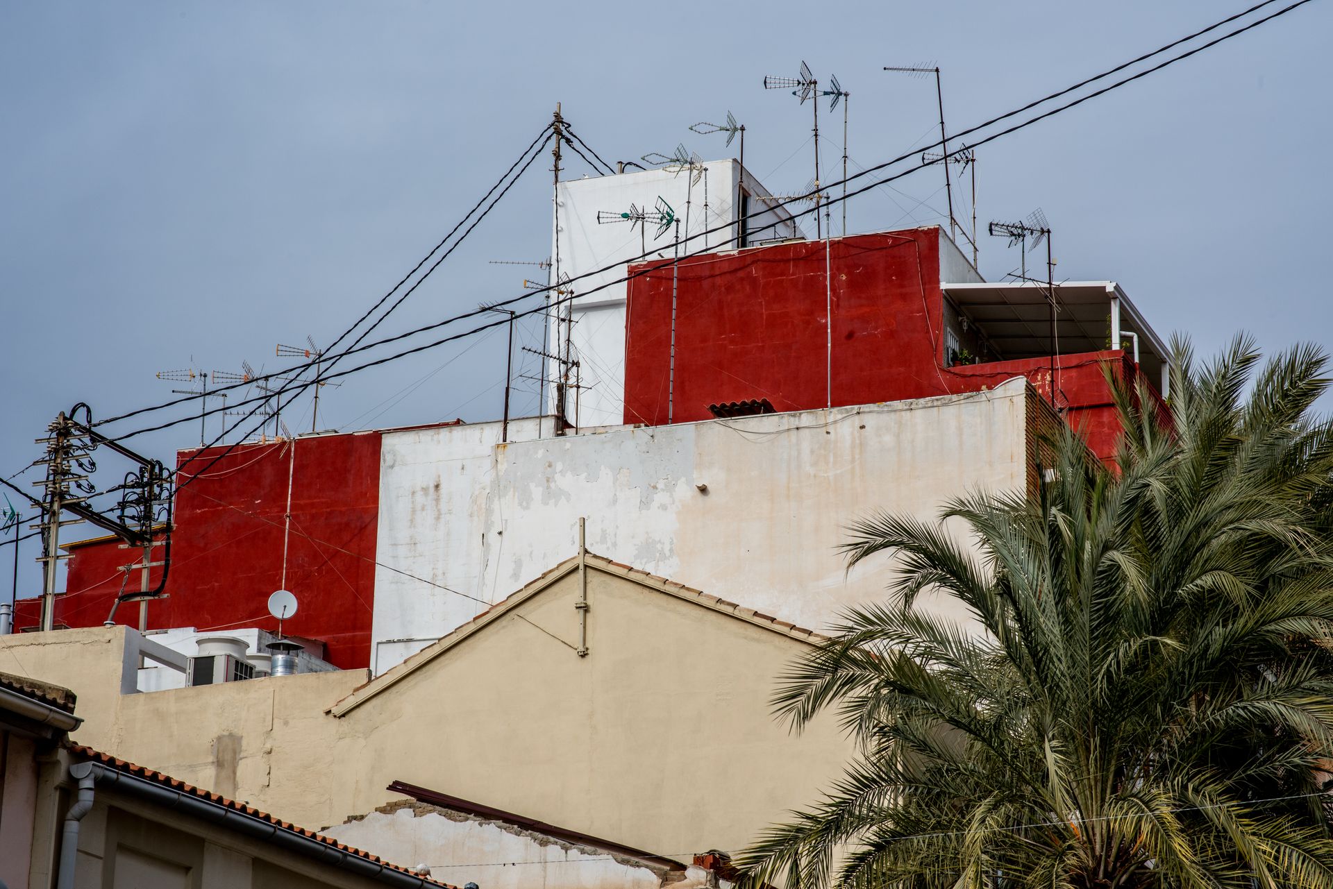 Colorful urban building with antennas and palm tree, under a clear sky.