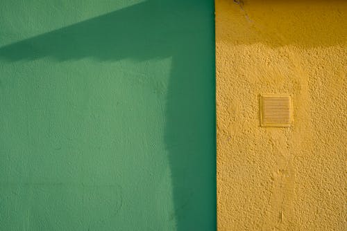 Free A vibrant street wall showcasing bold green and yellow textured surfaces with shadow play. Stock Photo