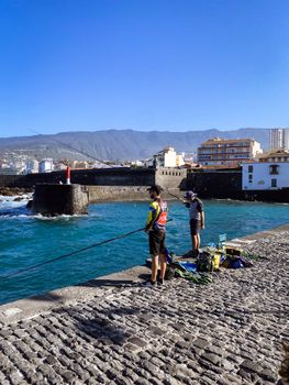 Two people enjoy fishing on the scenic coastline of Puerto de la Cruz, Tenerife.